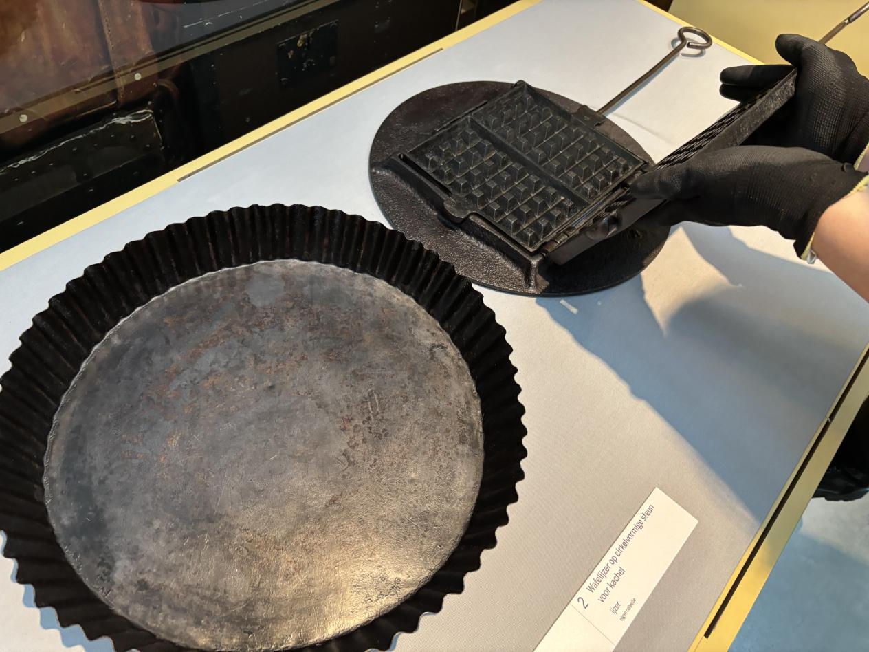 Handen met handschoenen plaatsen het wafelijzer terug in de vitrine