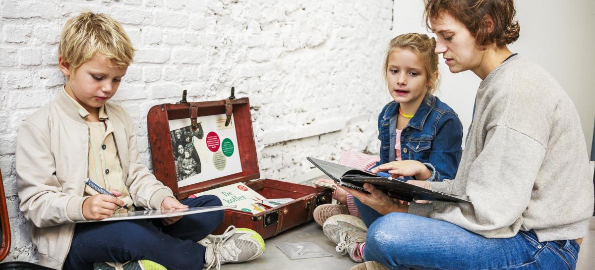 Een moeder zit met twee kinderen op de vloer en leest uit een boekje voor