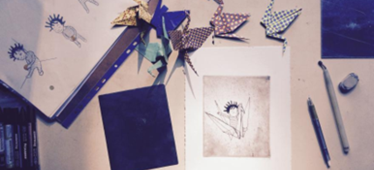 Foto van een bureau waarop illustraties liggen en kraanvogels in origami staan