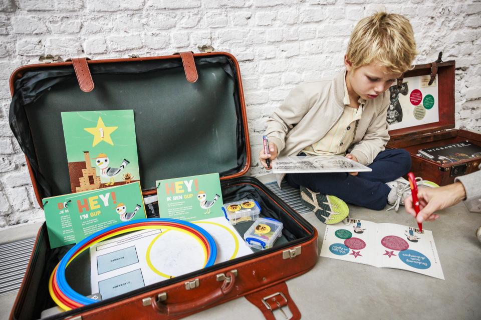Een kleuter zit op de grond bij een koffer