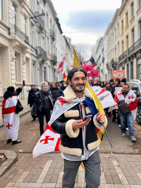 Een man staat met een Georgische vlag rond zich op straat