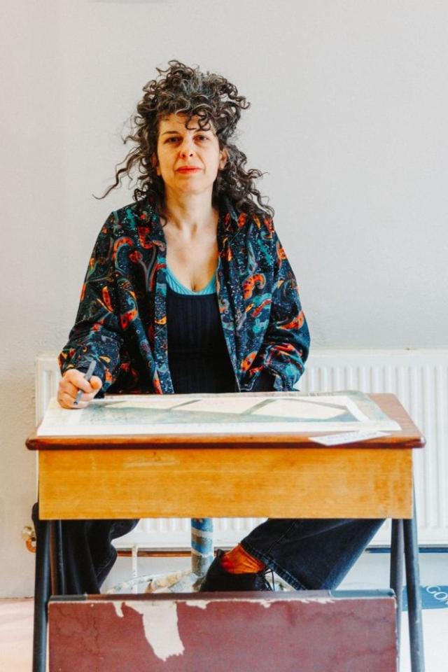 Foto van een vrouw met zwarte krullen die achter een tafel zit