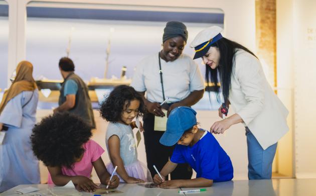 Een mama met drie kindjes krijgen uitleg in het museum van een gids met een zeekapiteinspet