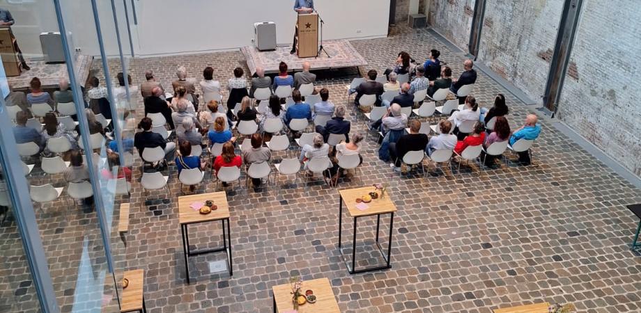 Overzichtsfoto van een loods met staantafels en een publiek