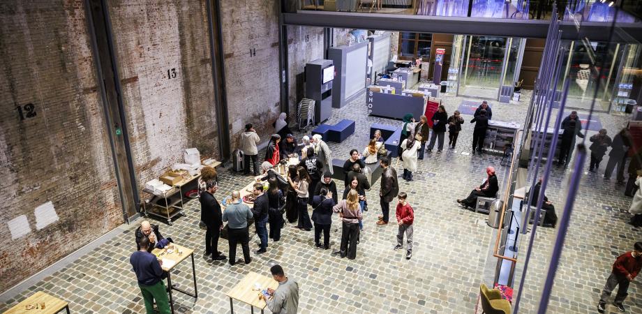 Foto in vogelperspectief van de loods waar mensen aan tafeltjes staan