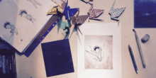 Foto van een bureau waarop illustraties liggen en kraanvogels in origami staan
