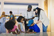 Een mama met drie kindjes krijgen uitleg in het museum van een gids met een zeekapiteinspet